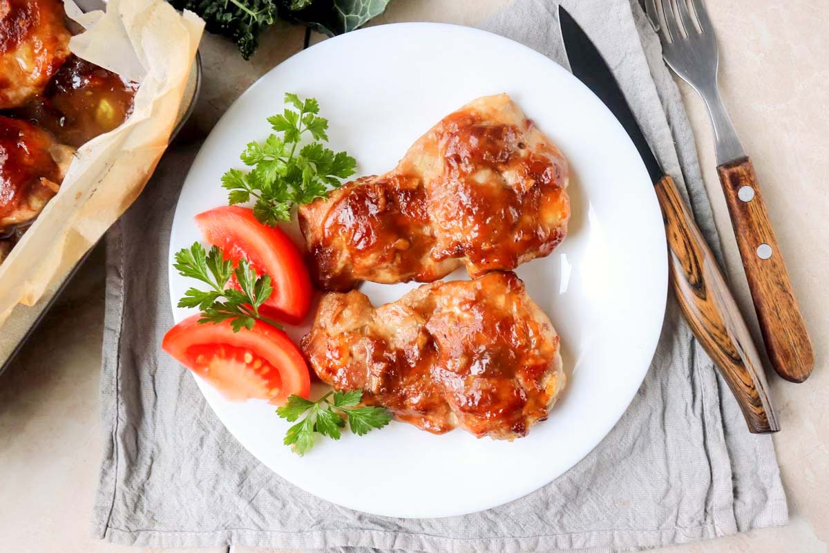 Chicken thighs on a plate garnished with parsley and tomato.