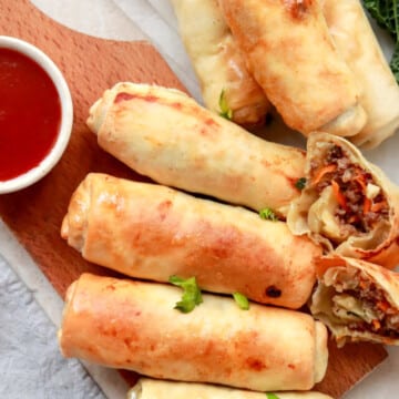 Egg rolls on a cutting board with dipping sauce.