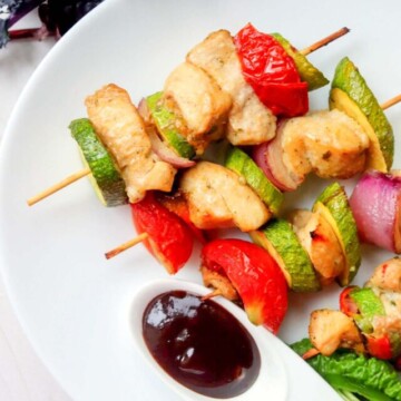 chicken kabobs on a plate with dipping sauce.