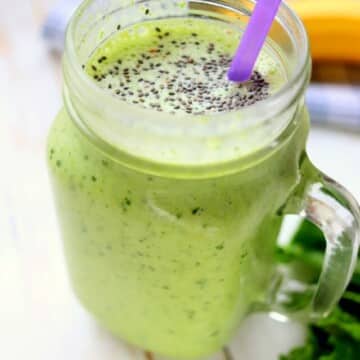 Green smoothie in a mason jar with a purple straw.