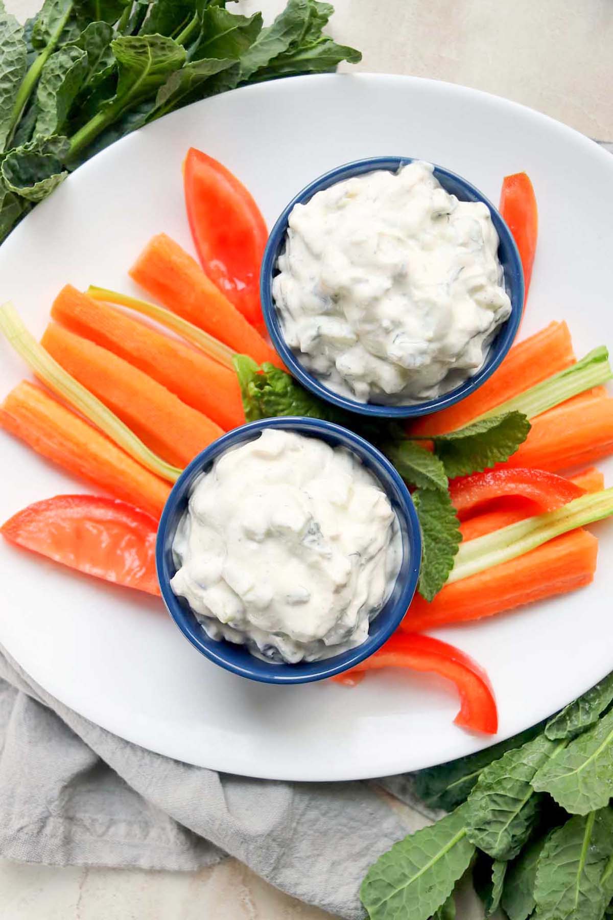 Two cups of dip on a plate with carrots sticks.