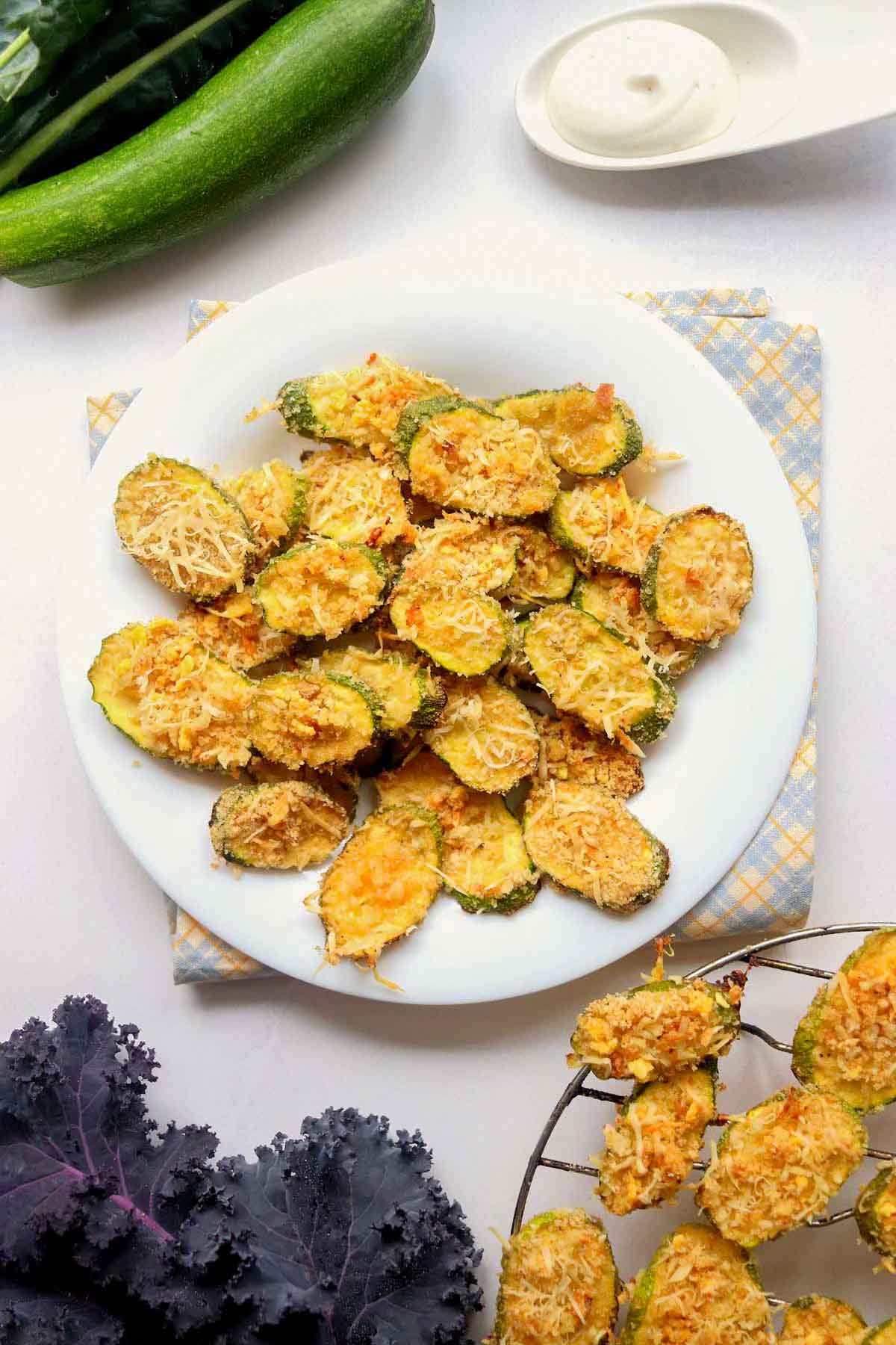 Zucchini chips on a plate that is set on a kitchen towel.