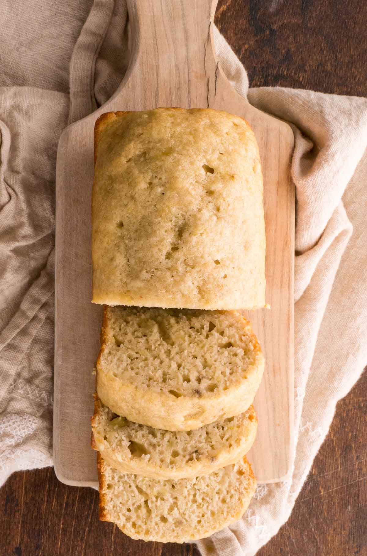 Sliced banana bread on a cutting board that is sitting on a kitchen towel.