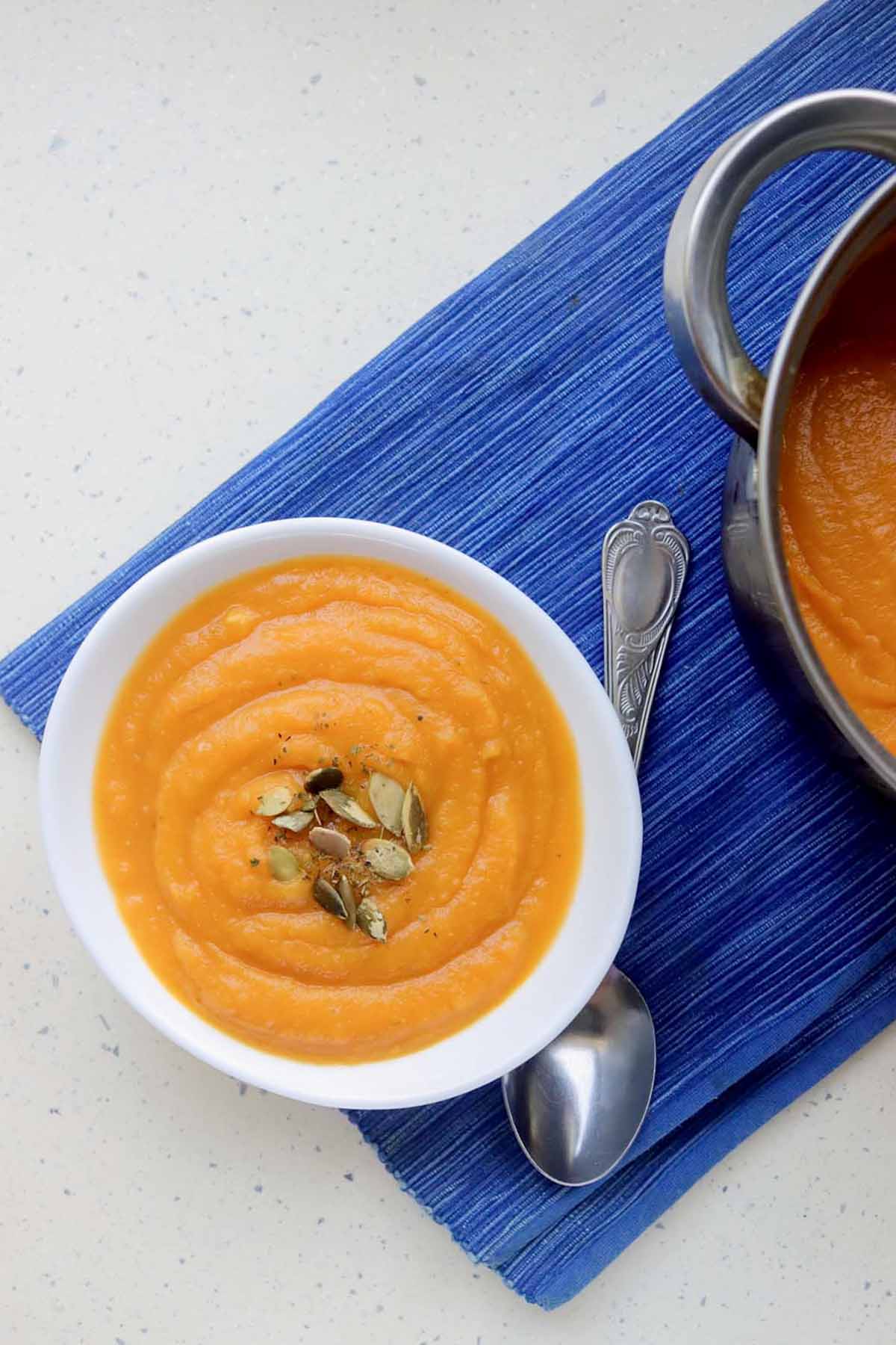 bowl of pumpkin soup next to a pot.