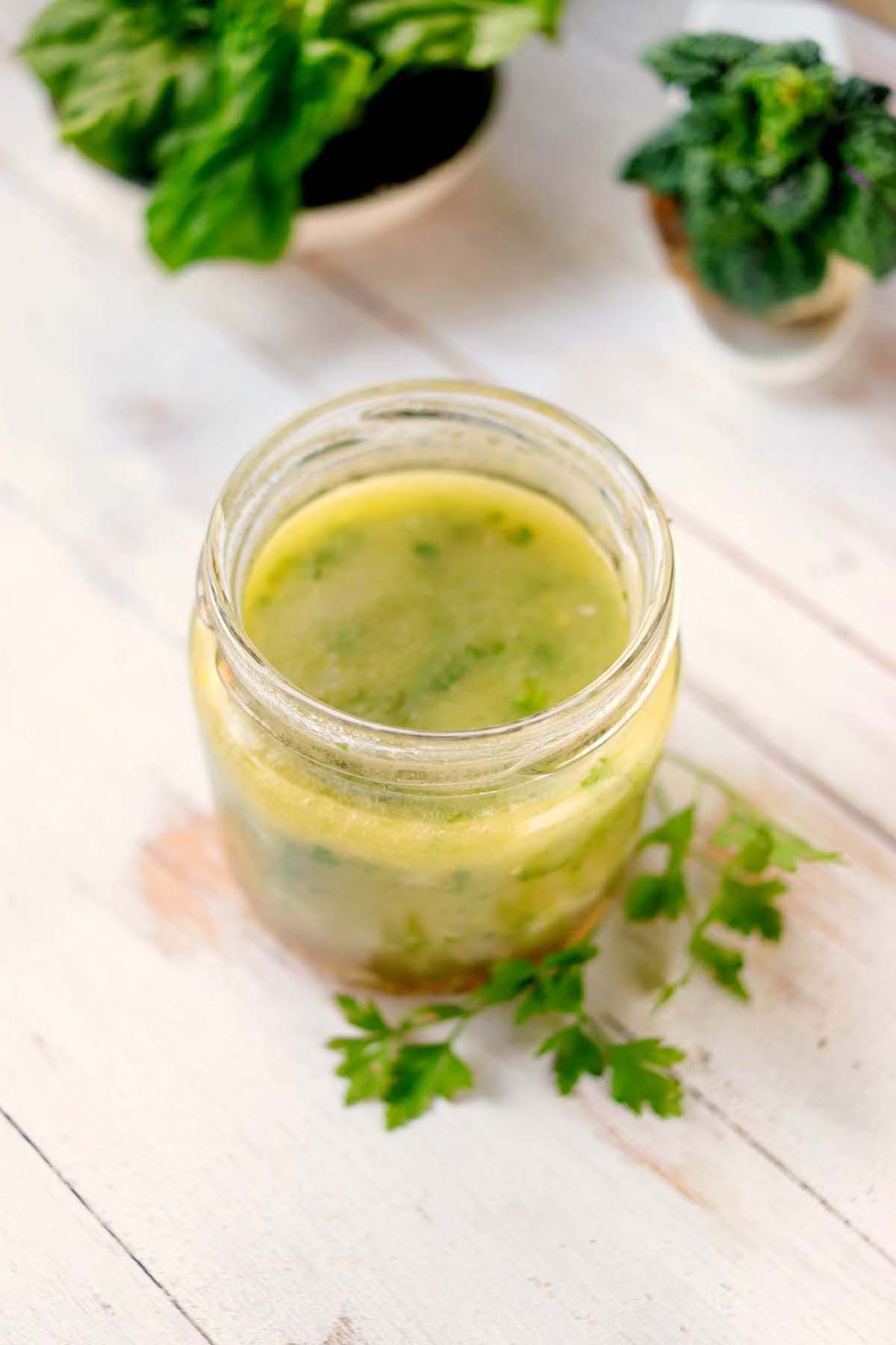 Vinaigrette in a jar next to a sprig of parsley. 