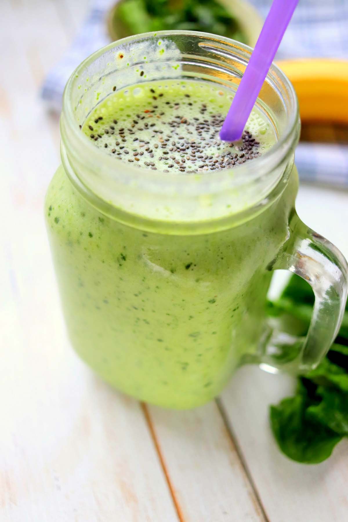 Green smoothie in a mason jar with a purple straw.