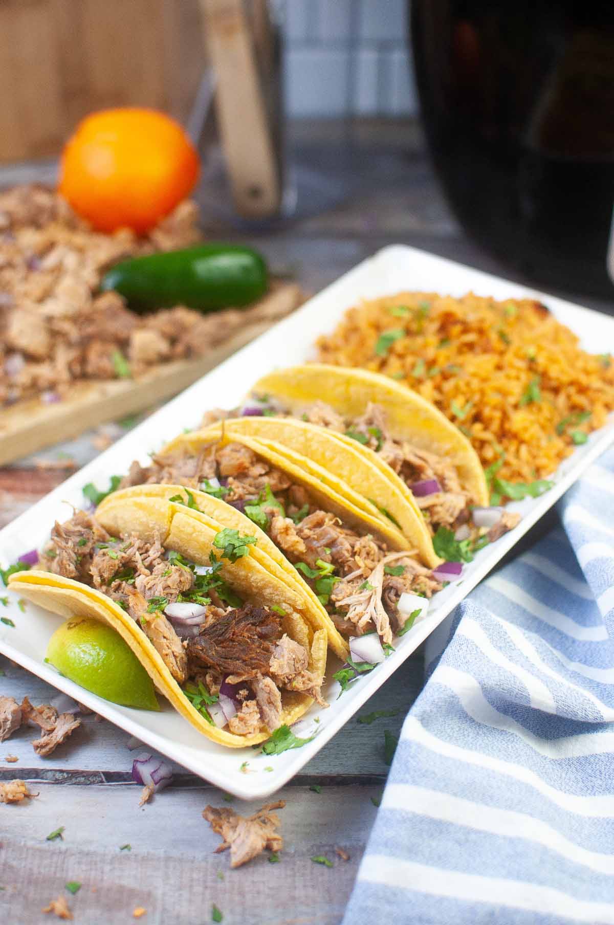 carnitas tacos on a plate with rice and a lime wedge.