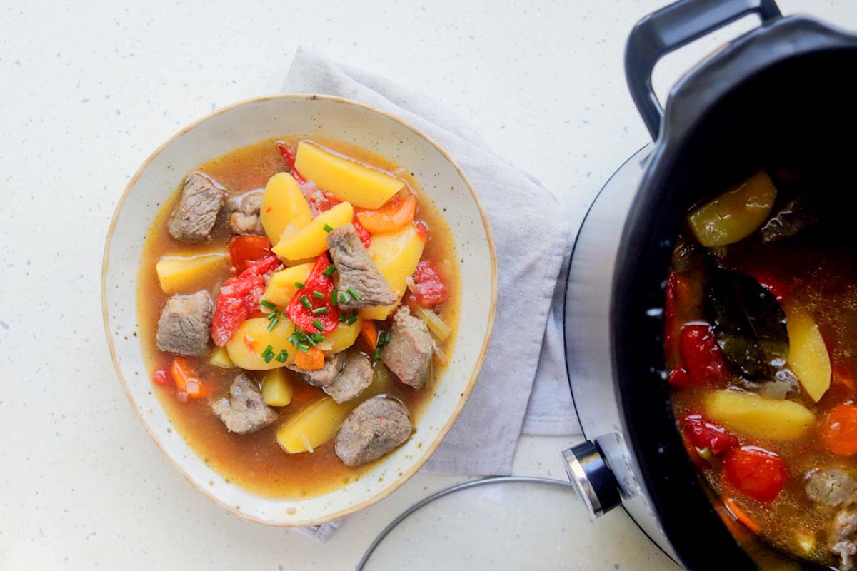 Beef stew in a bowl next to the slow cooker.