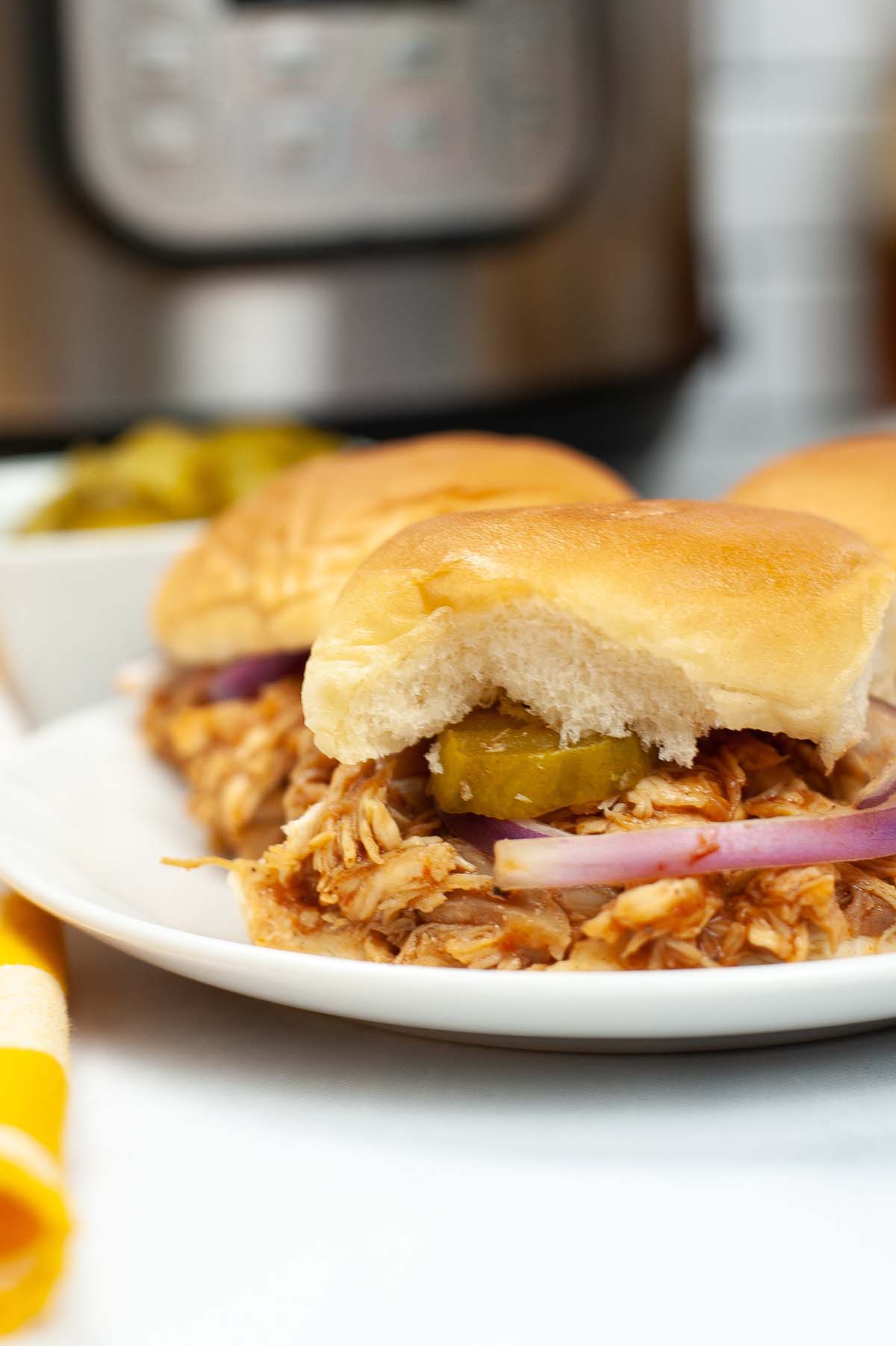 chicken sliders on a plate topped with pickles and onion.