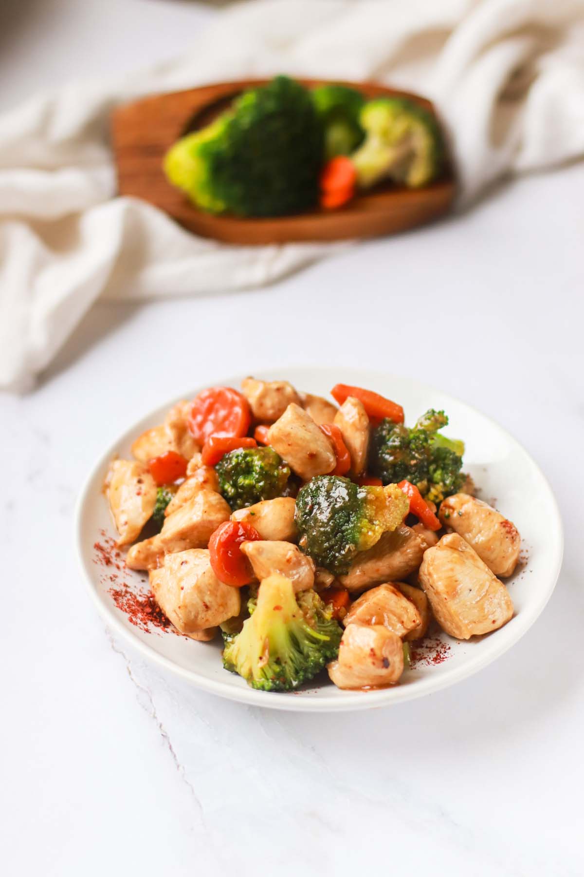 Teriyaki chicken on a plate next to a cutting board with vegetables.