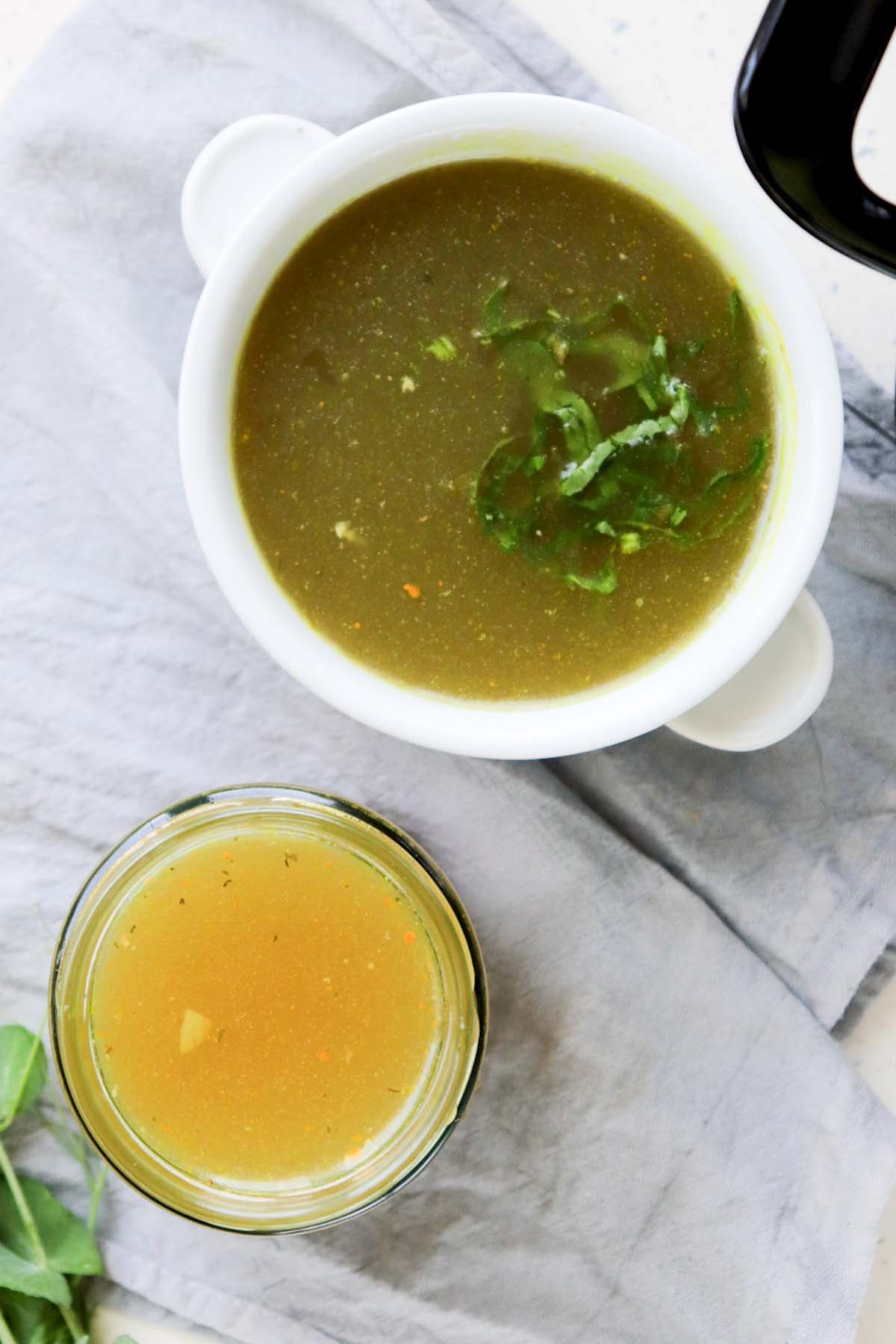 Stock in a jar and a bowl on a kitchen towel.