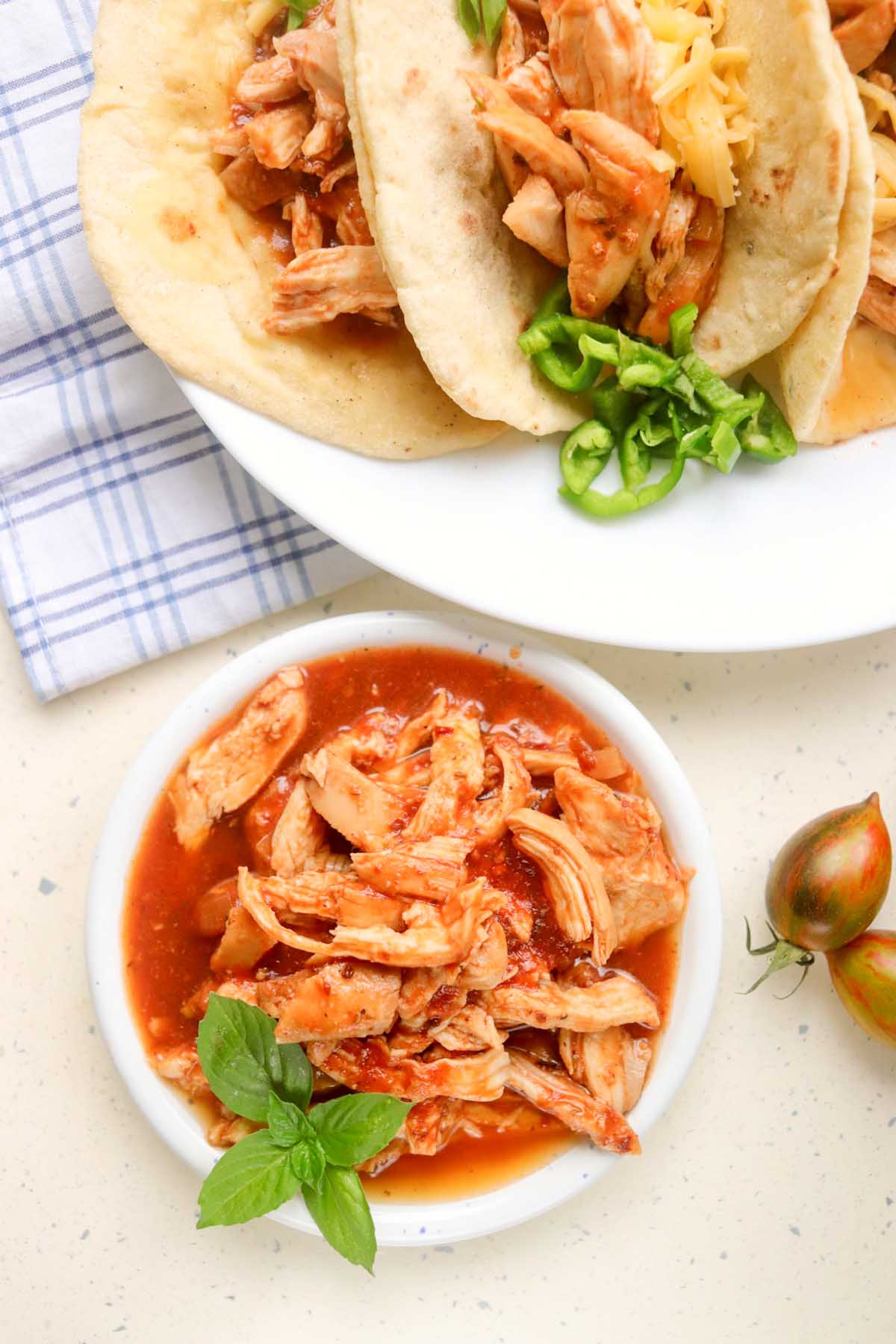 Chicken tacos on a plate next to a bowl of pulled chicken.