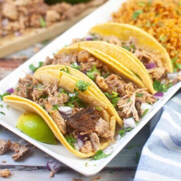 carnitas tacos on a plate with rice and a lime wedge.