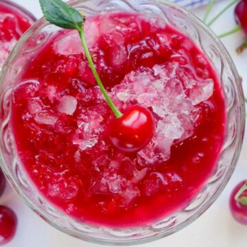 cherry snow cone in a glass topped with a cherry.