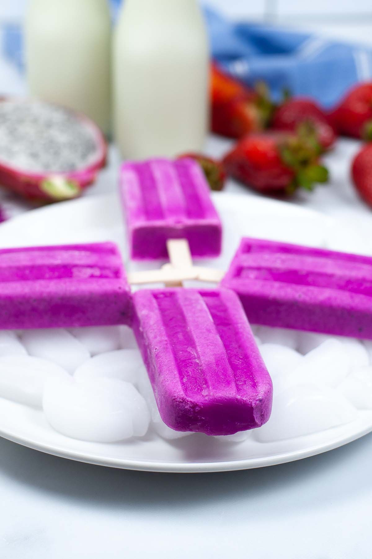 four dragon fruit popsicles on a plate with ice.