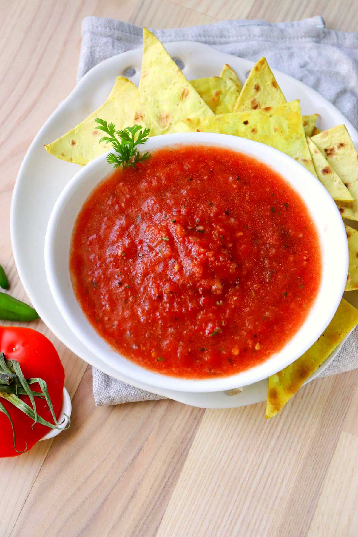 salsa in a bowl with tortilla chips on a plate.