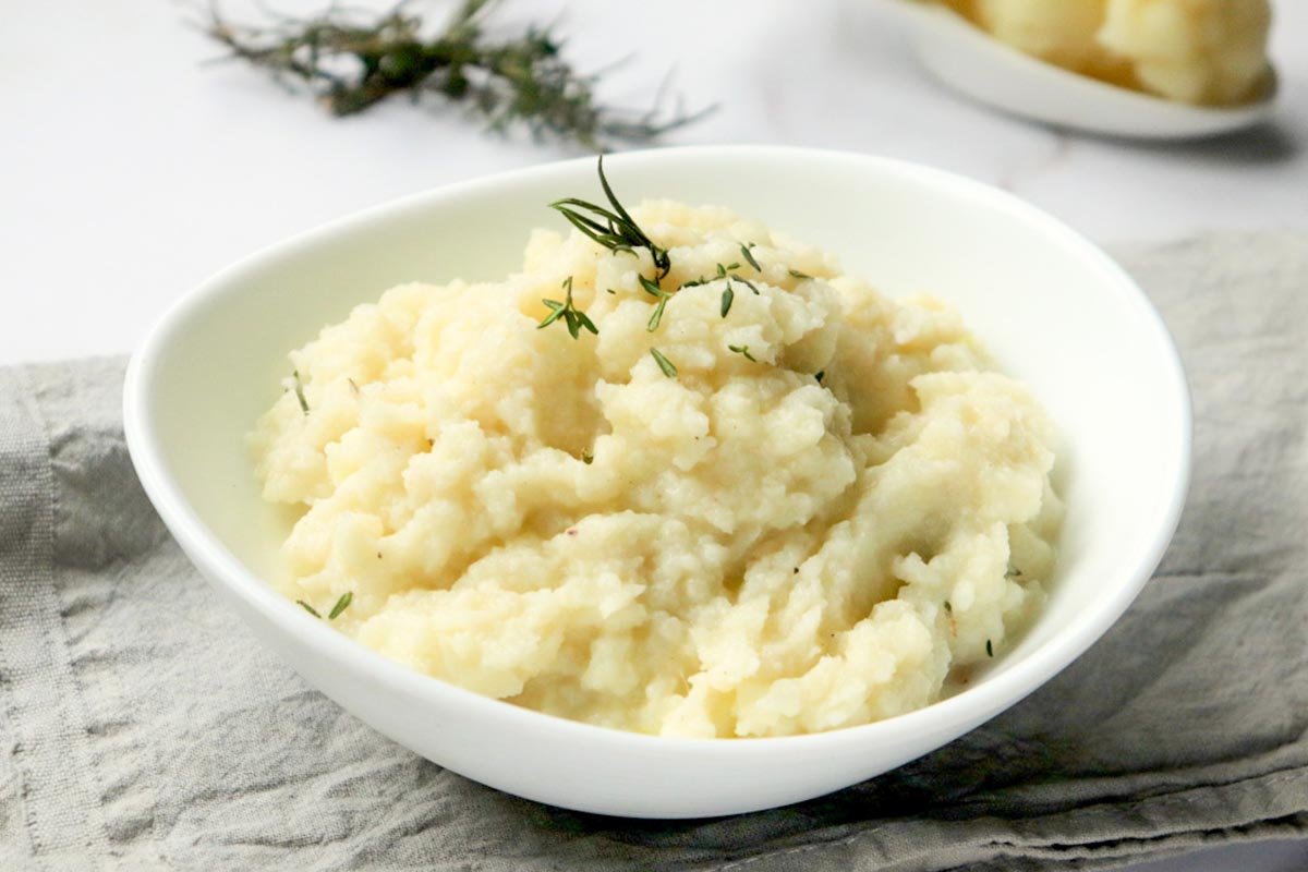 Mashed cauliflower in a bowl set on a kitchen towel.