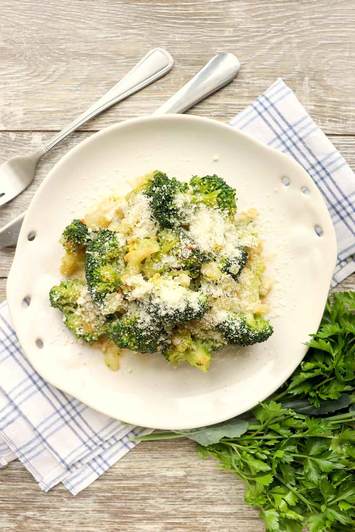 Broccoli on a plate next to a bunch of parsley.