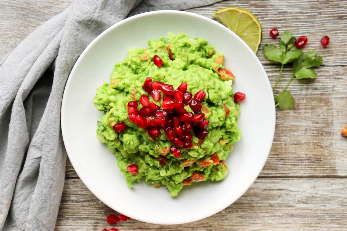Guacamole on a white bowl set on a wood table.