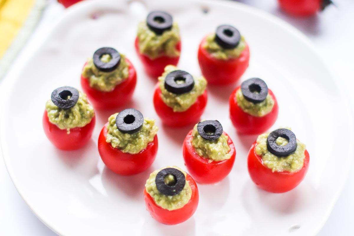guacamole stuffed cherry tomatoes on a white plate.