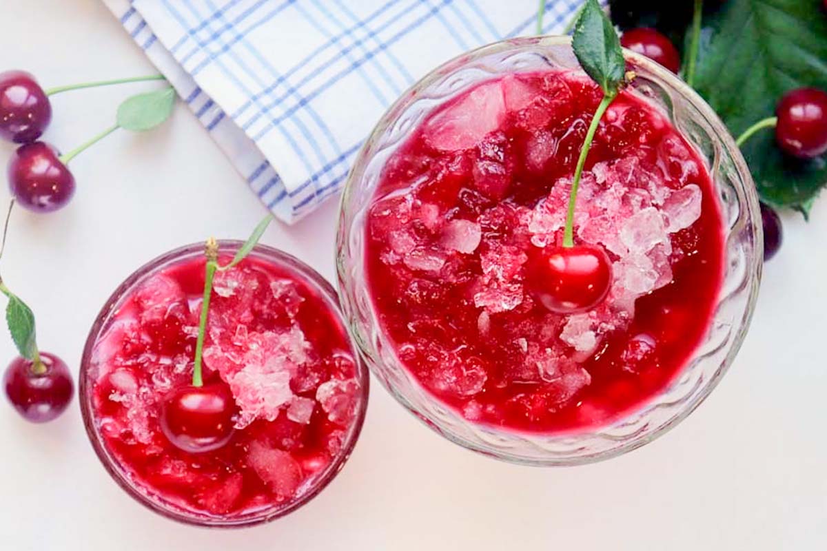 Two dishes of snow cones topped with cherries.