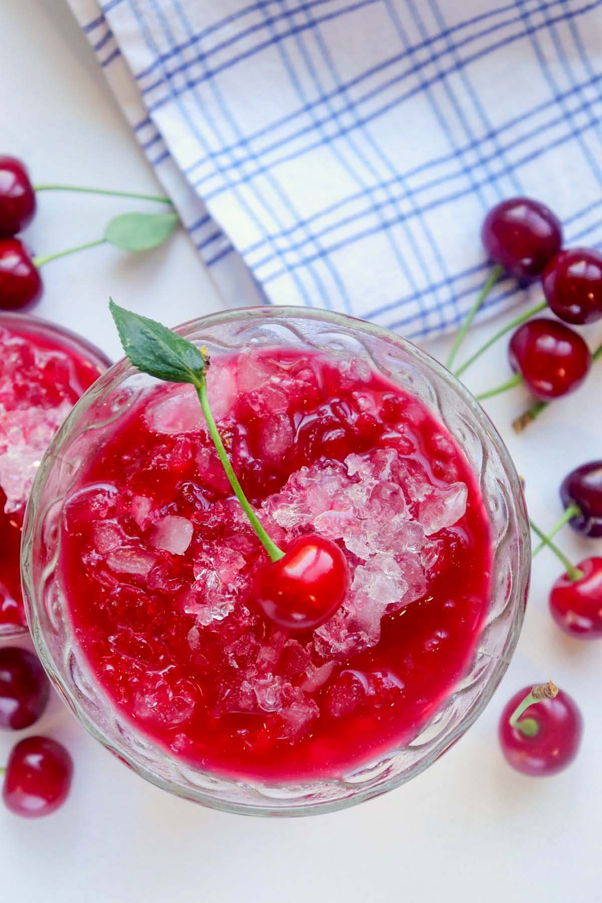 Cherry snow cone in a glass topped with a cherry.