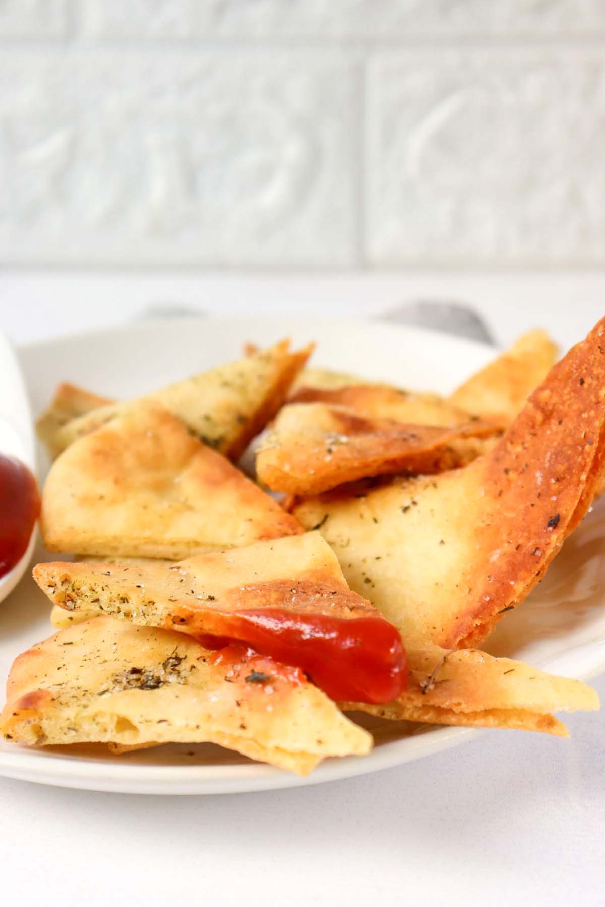 Pita chips on a plate and one chip dipped in ketchup.