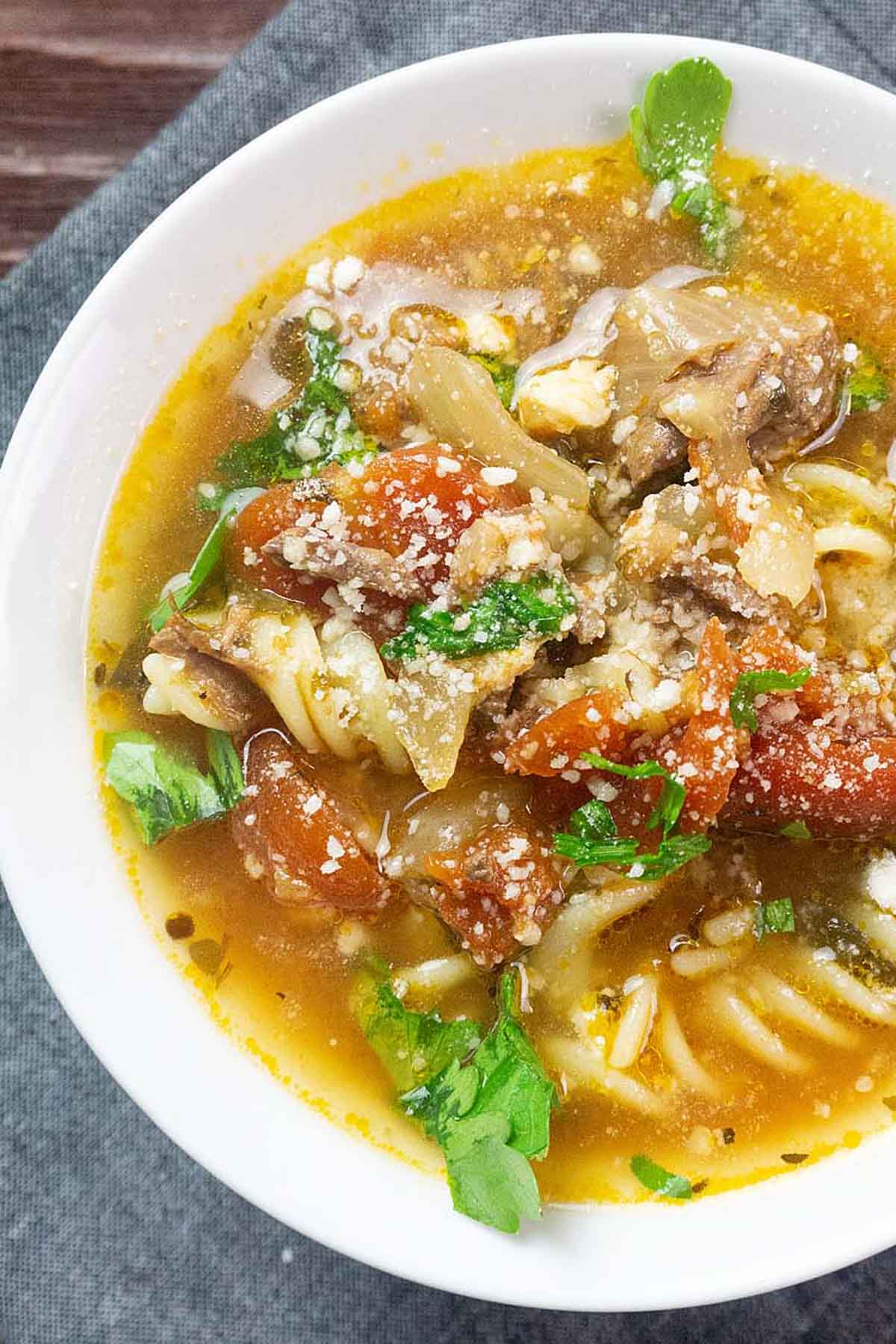 Beef and noodles in a bowl topped with parmesan cheese.