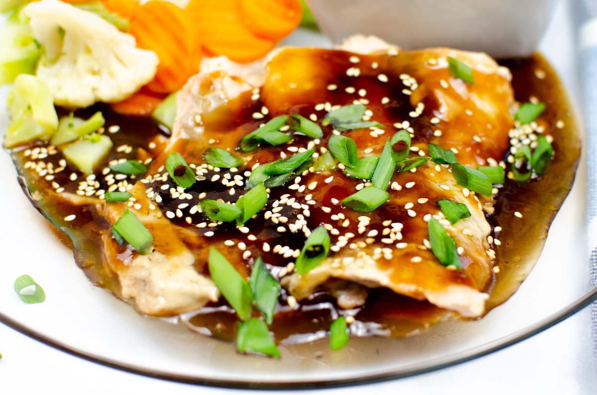 Salmon on plate topped with teriyaki sauce and chopped green onions.