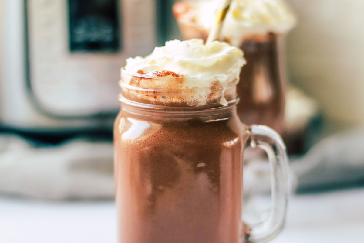 Hot chocolate in a glass with whipped cream and a straw.