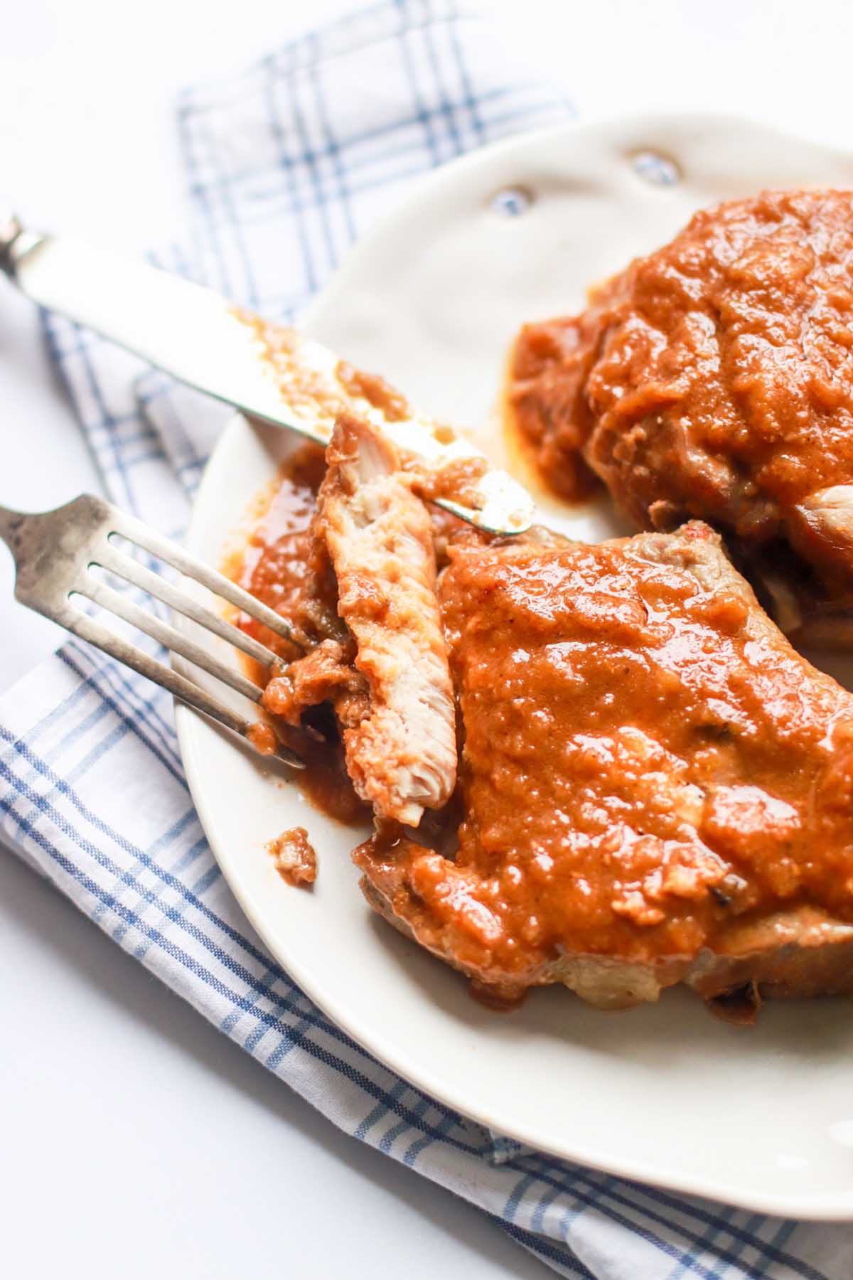 Pork chop cut in half next to a fork and knife.