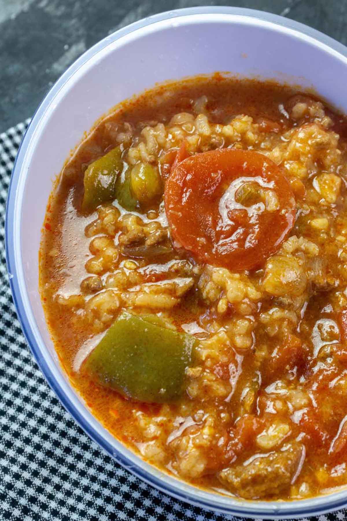 Soup topped with tomatos and green bell pepper chunks.