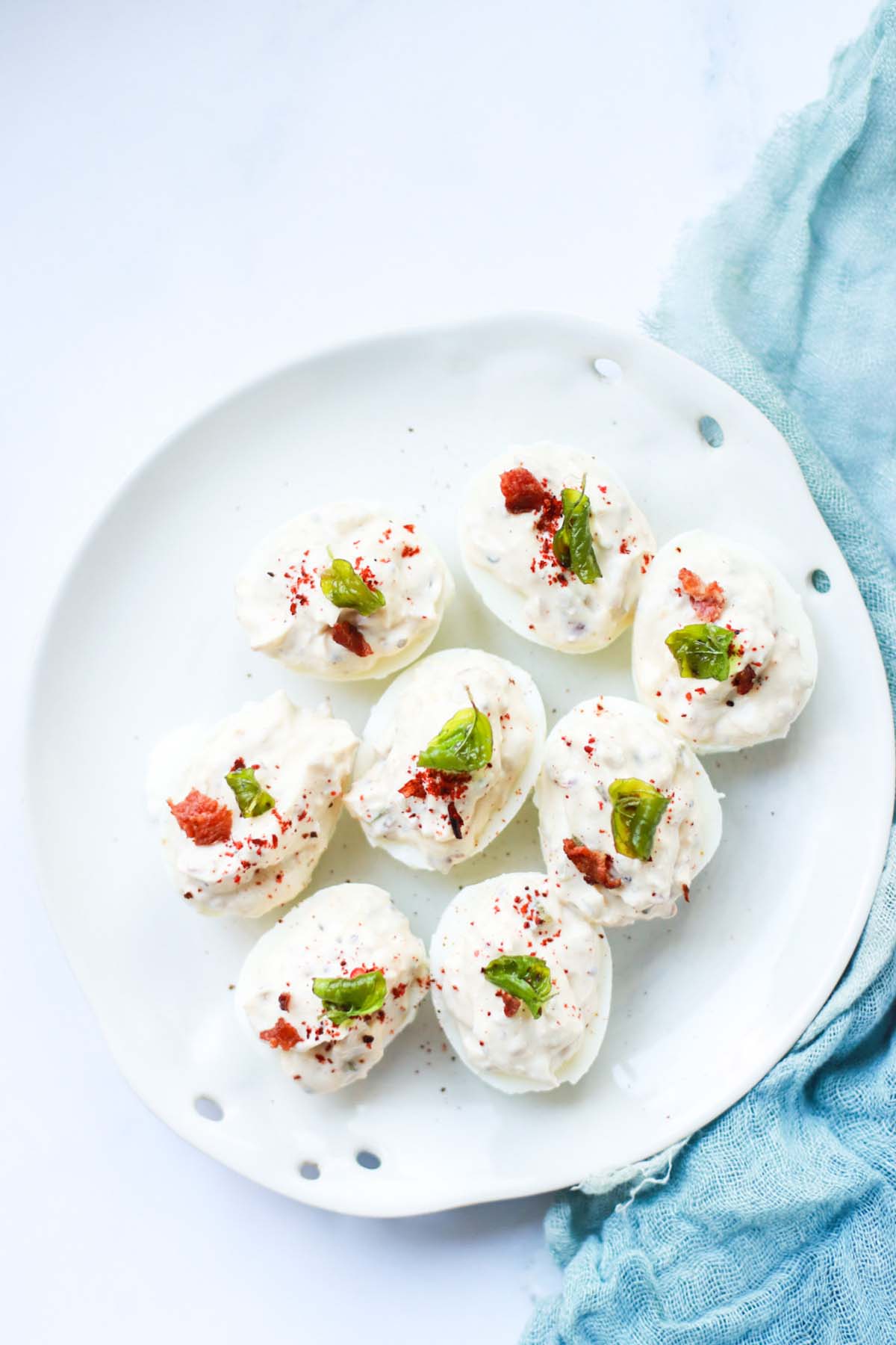 Deviled eggs on a white plate next to a blue kitchen towel.