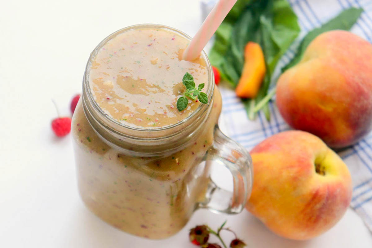 Smoothie in a jar next to a kitchen towel and peaches.