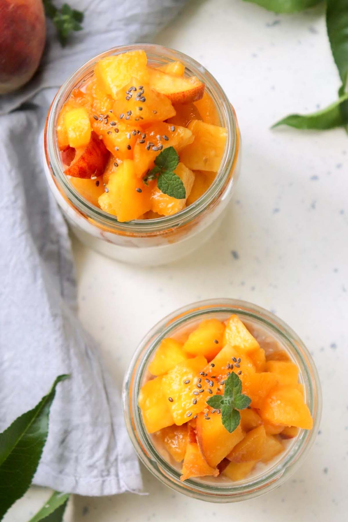 Two jars filled with oats and topped with peaches.