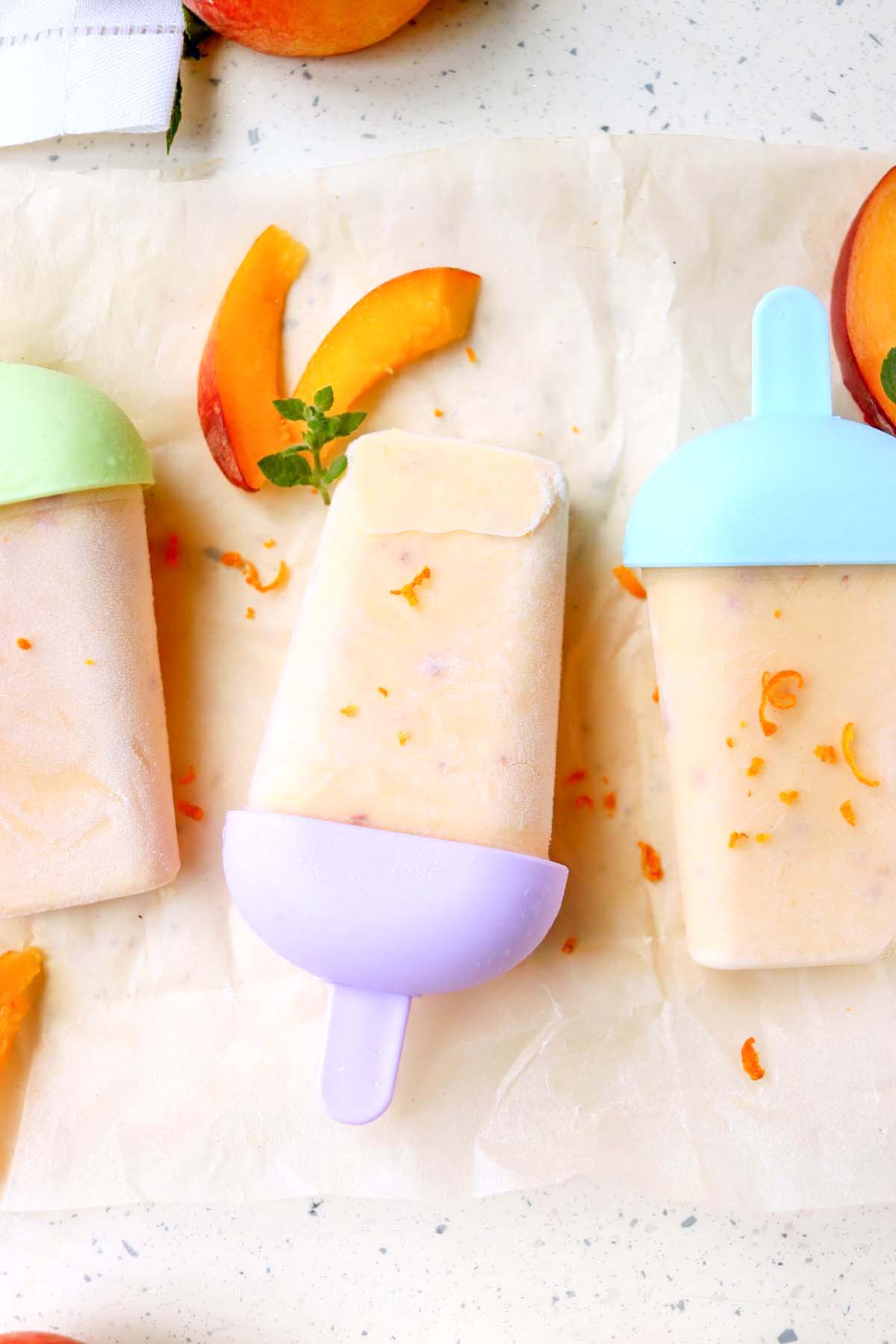 Popsicles and peach slices on parchment paper.