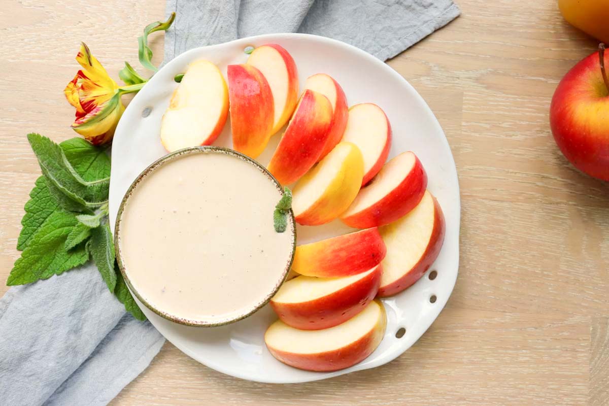 A plate with sliced apples and dip on a blue kitchen towel.