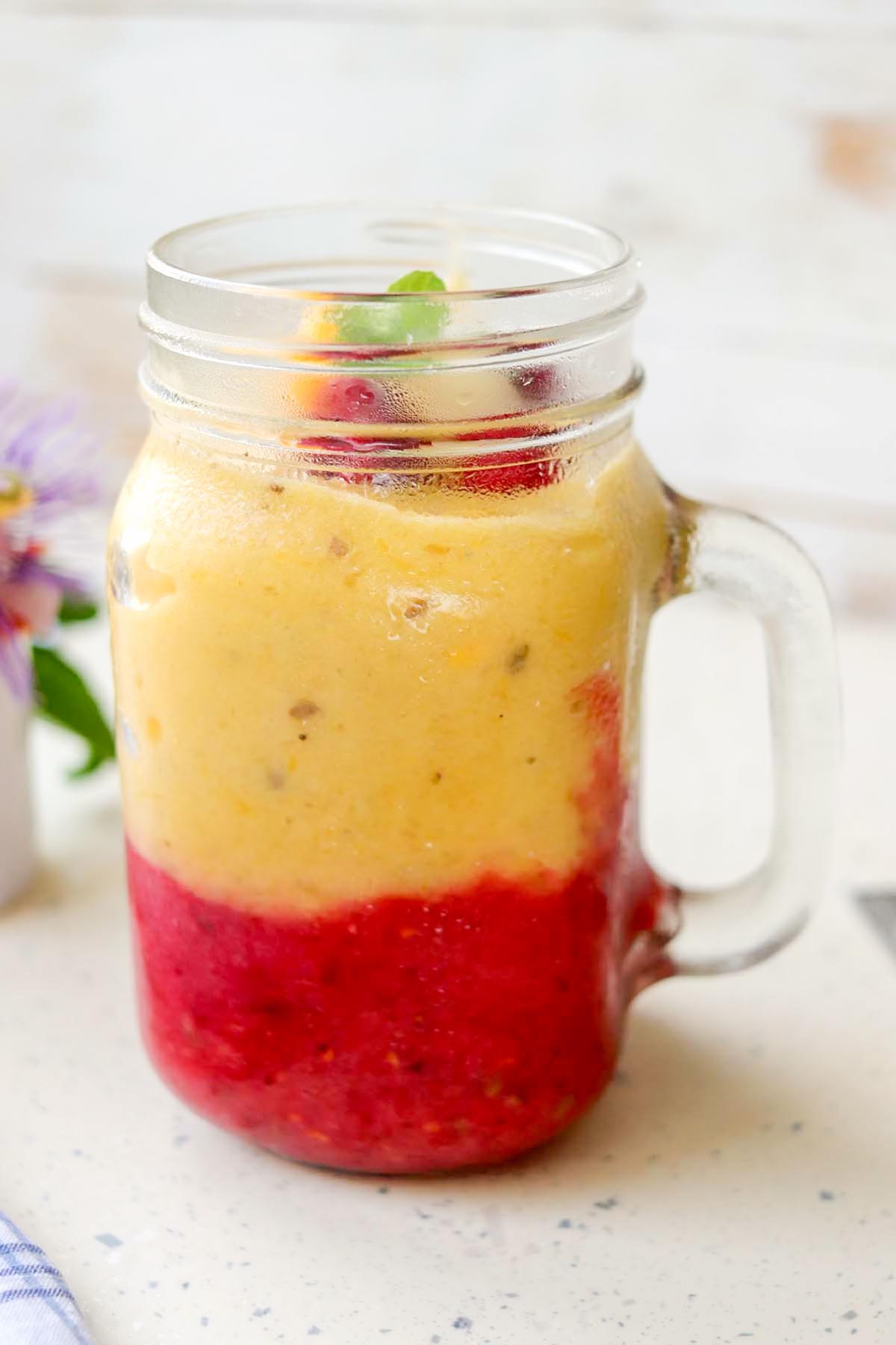 side view of pineapple raspberry smoothie in a glass jar.