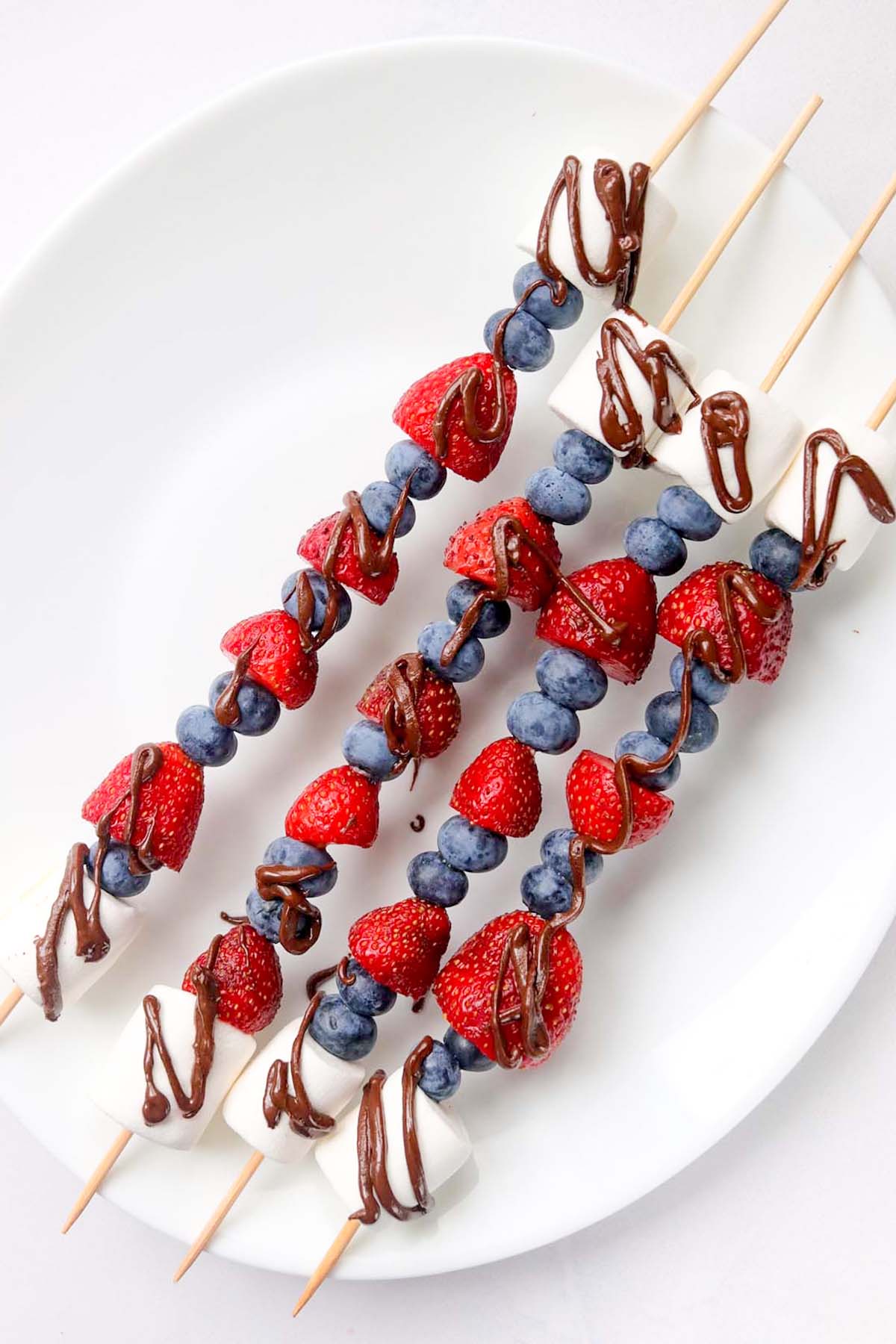 Four fruit kabobs on a white plate.