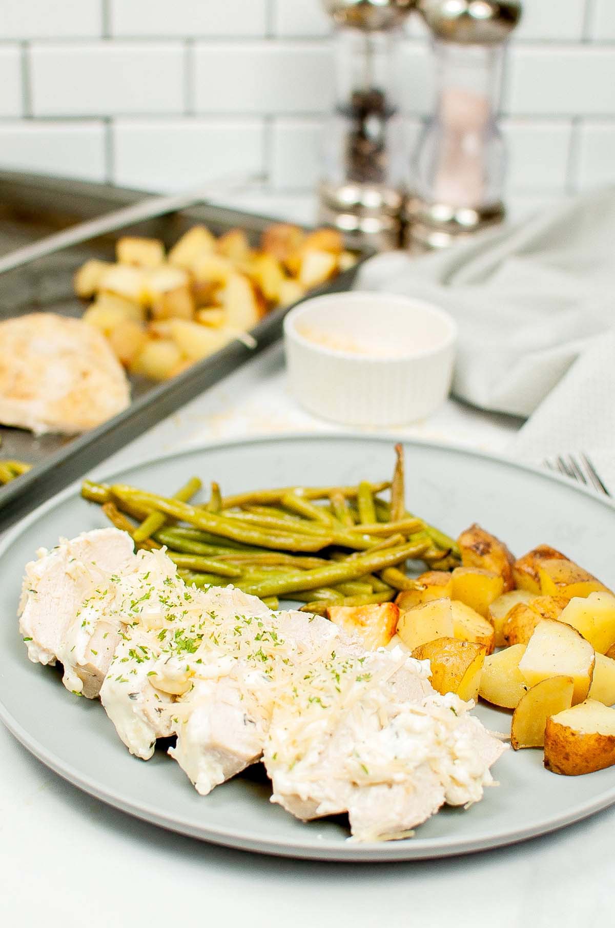 Chicken, potatoes and green beans on a plate next to the baking sheet.