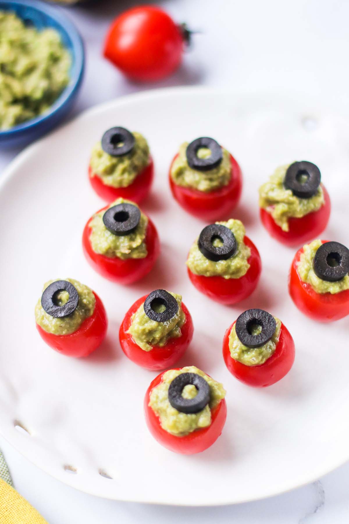 guacamole in cherry tomatoes on a white plate.