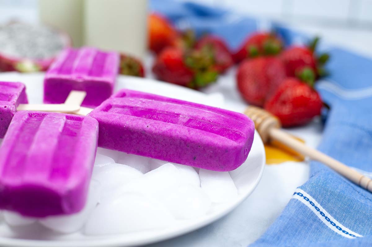 side view of dragon fruit popsicles on a plate of ice.