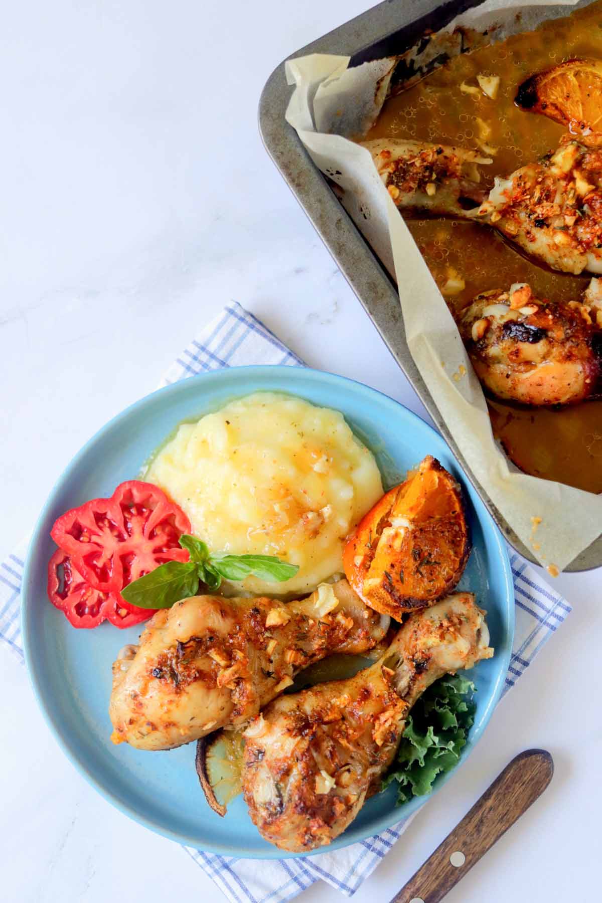 Drumsticks and mashed potatoes on a plate next to the baking dish.