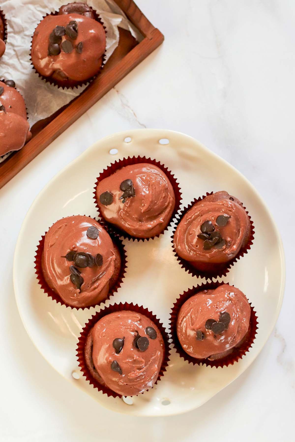 Chocolate cupcakes on a plate topped with frosting and chocolate chips.