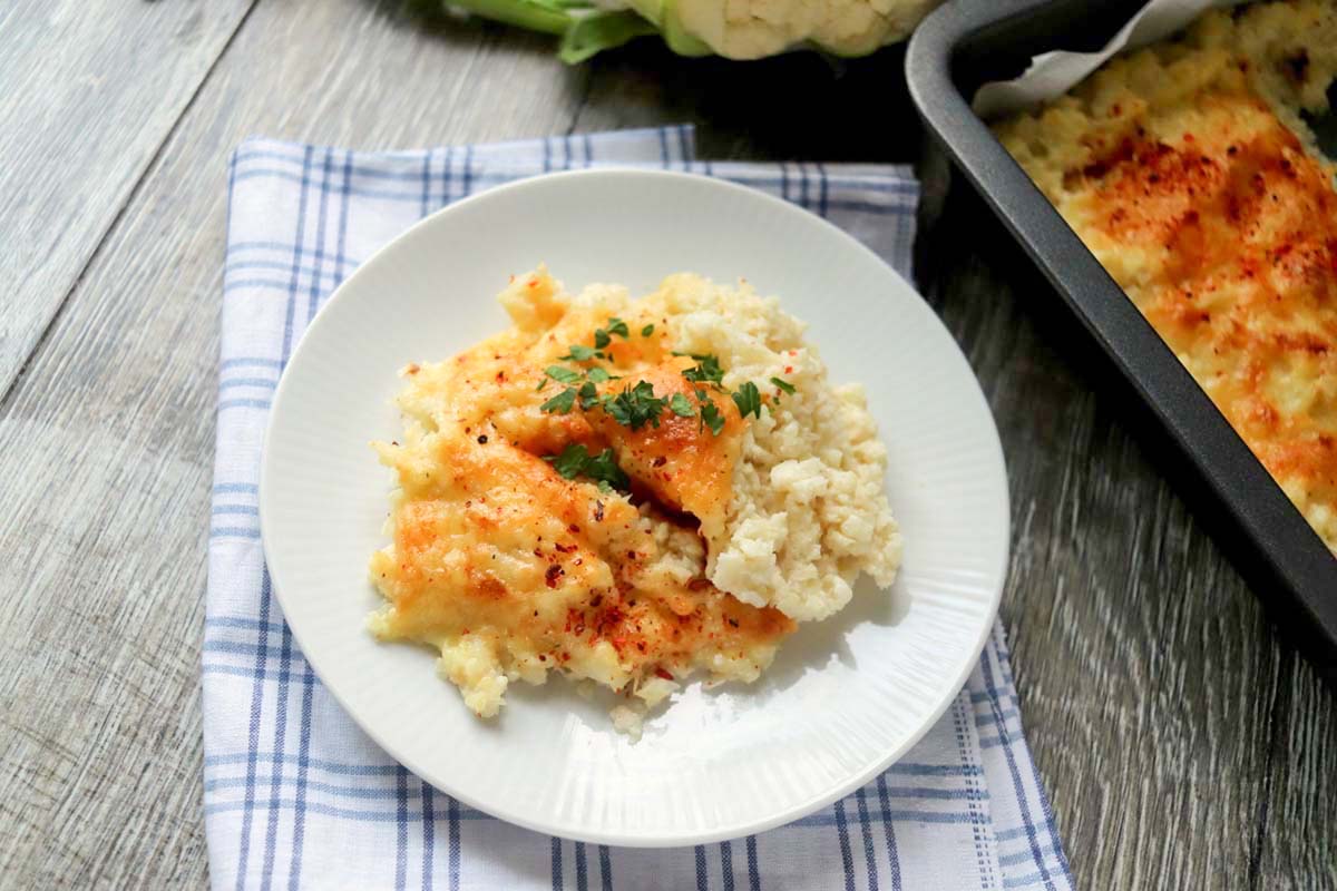 Cauliflower scooped on a plate next to a baking dish.