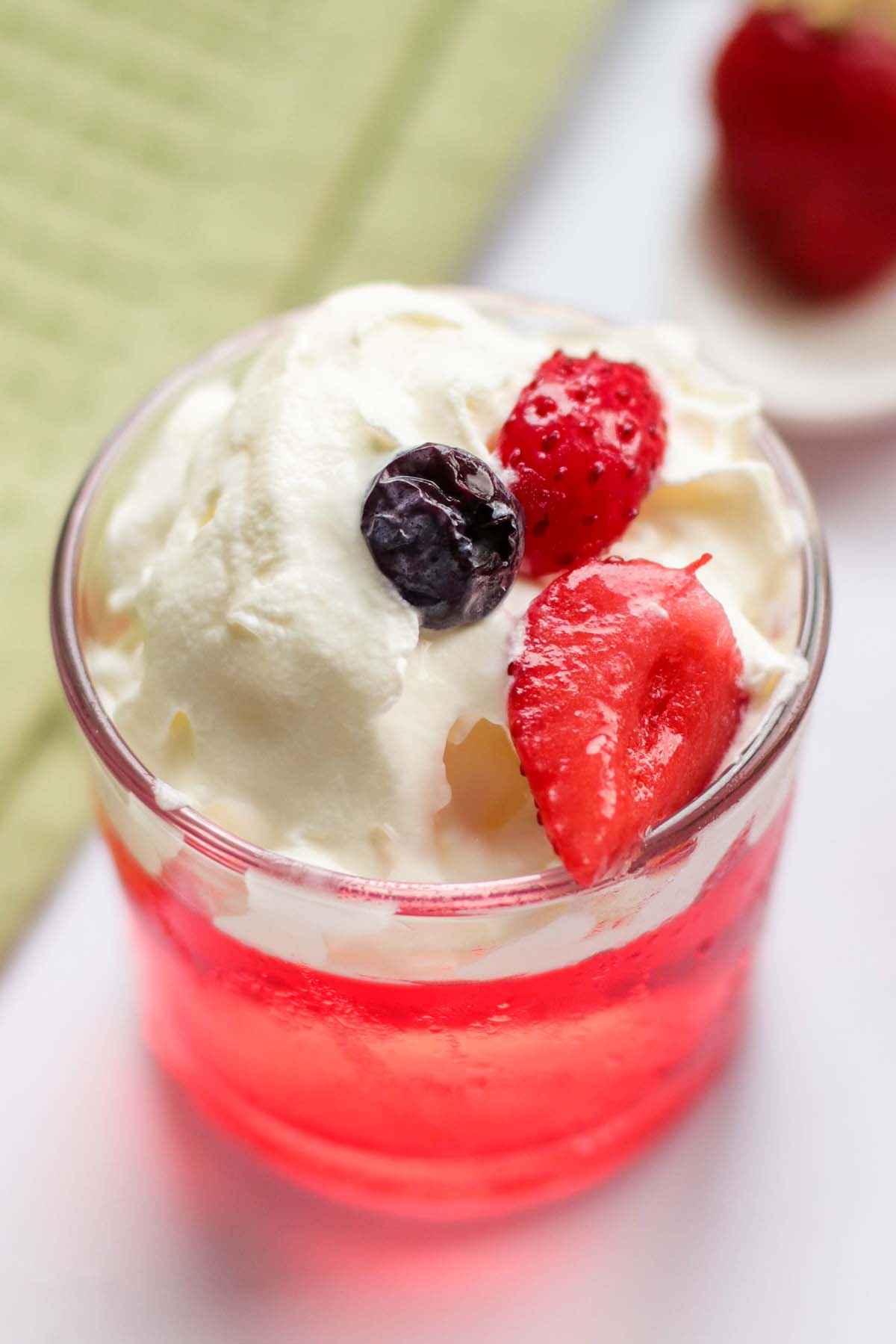 red jello in a glass topped with whipped cream.