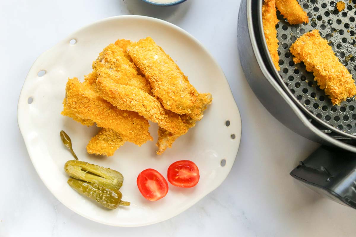 Cooked fish on a plate next to the air fryer.