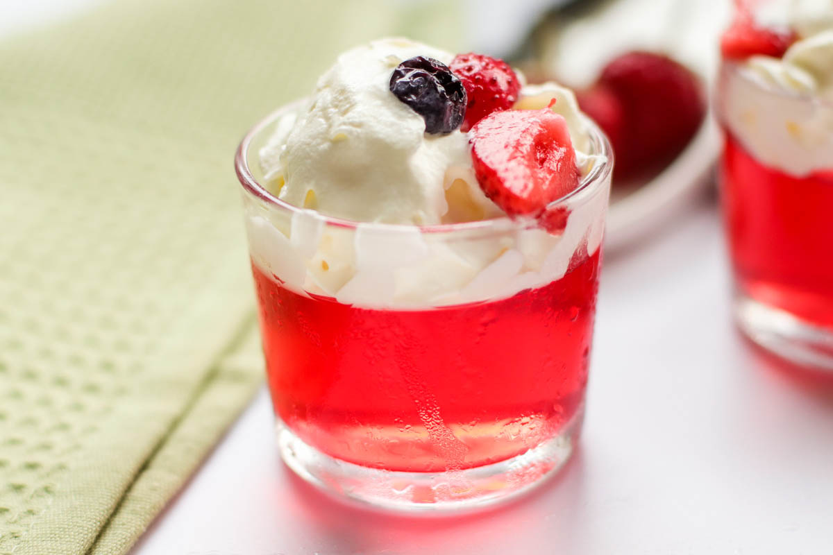 Red jello in a glass topped with strawberries and blueberries.