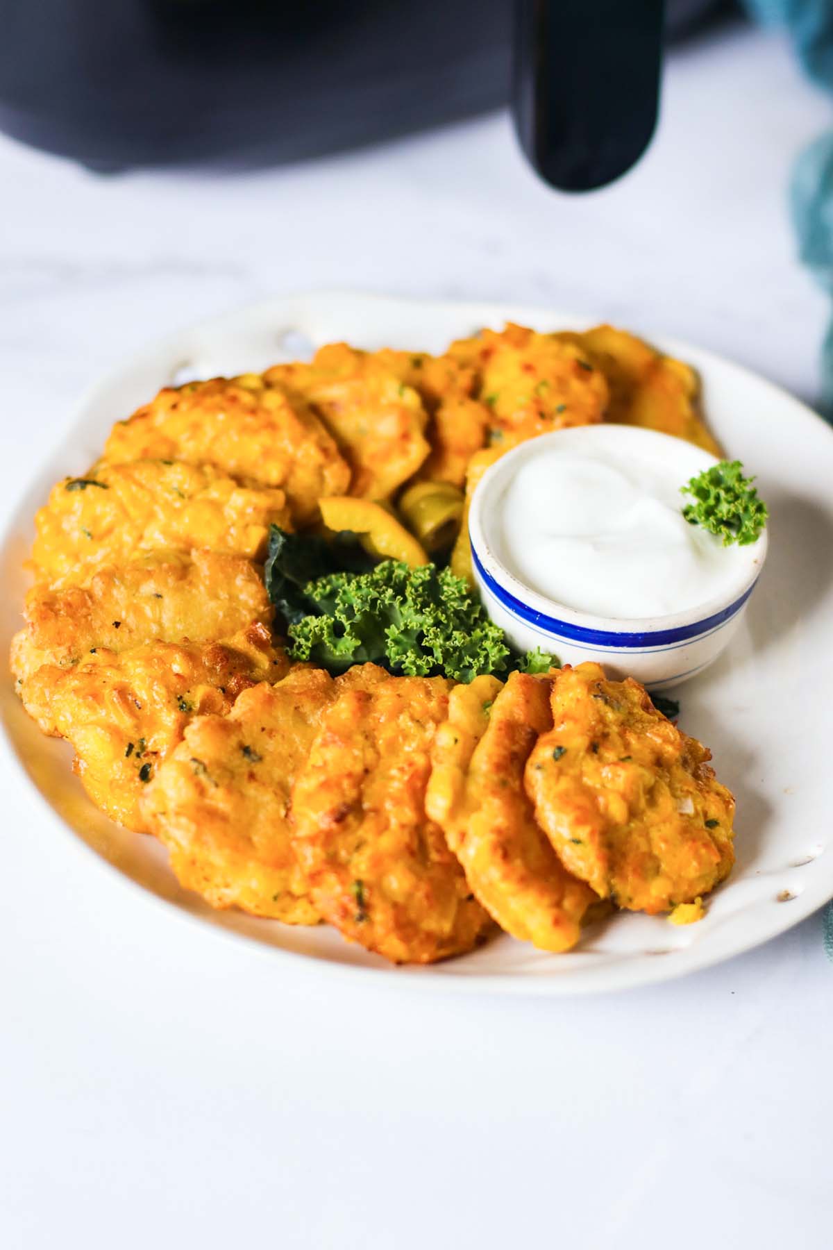 Fritters on a plate topped with parsley next to a dipping sauce.