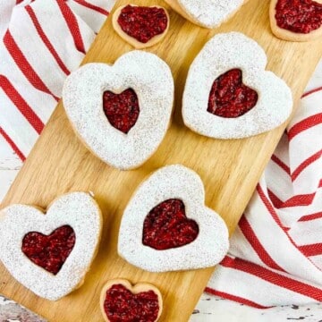 Heart shaped cookies on a board that is set on a kitchen towel.